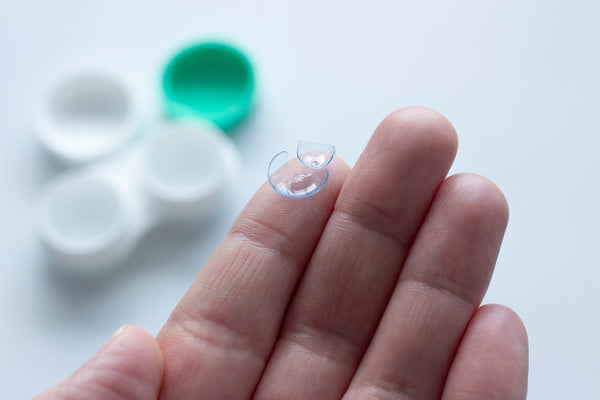 Broken contact lens resting on a person's fingertip with a white and green contact lens case in the background.