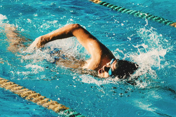 Swimmer wearing goggles and swim cap performing freestyle stroke in a pool with lane dividers and splashing water.