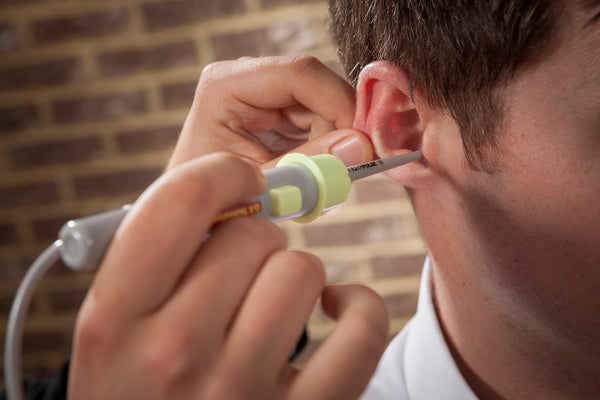 Close-up of a person using an ear cleaning tool to remove earwax from the ear canal against a blurred brick wall background.