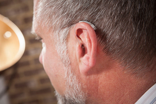 Close-up of a person wearing a behind-the-ear hearing aid with a thin tube and earmold.