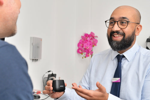 Audiologist holding a hearing aid charger and smiling while talking to a patient during a hearing test.