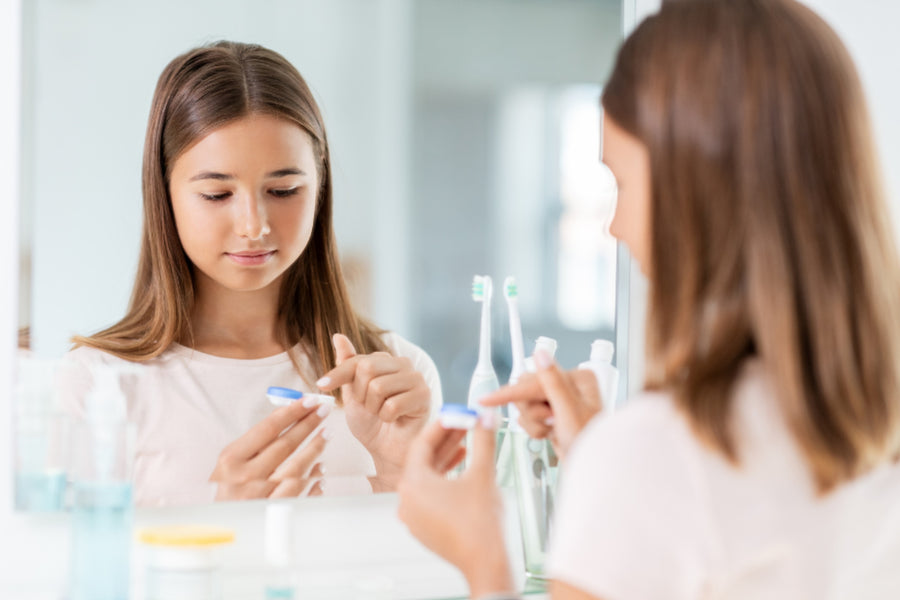 young girl getting ready to put contact lens in, in front of a mirror