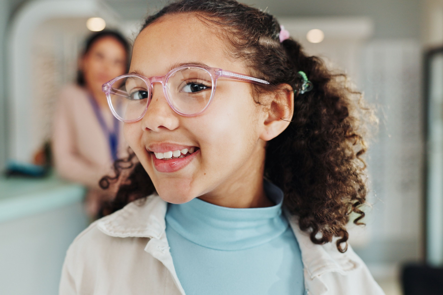 Smiling child wearing pink eyeglasses and seeing how they look.