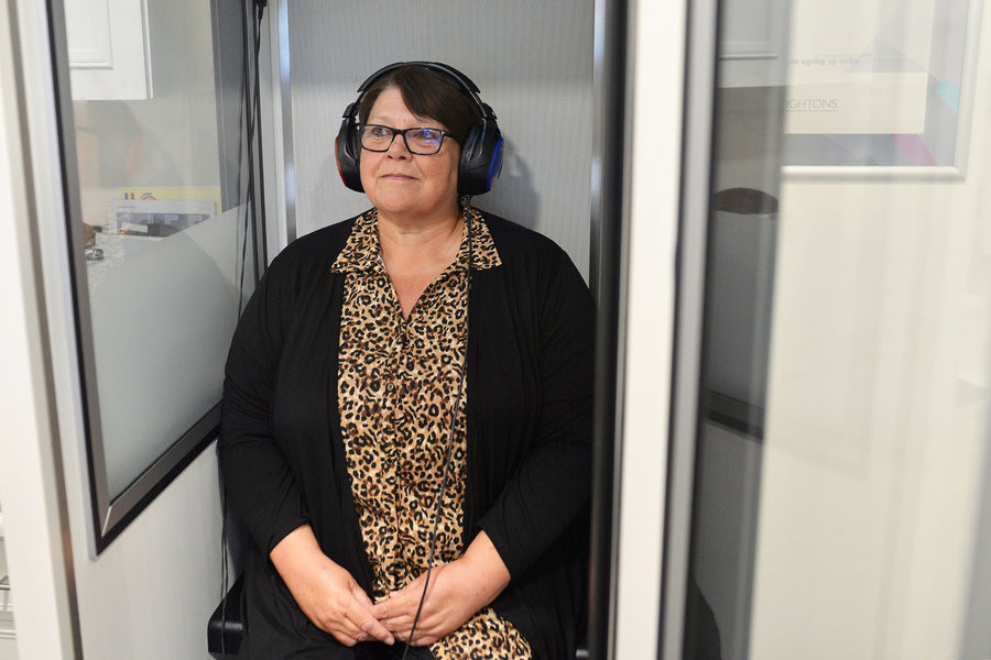 lady sat in a booth having a hearing test with over ear headphones on