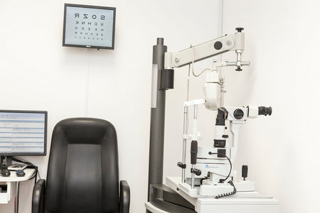 Ophthalmological examination setup with chair, slit lamp, and eye chart on a white wall.