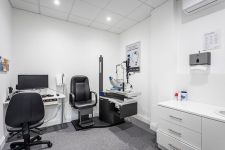 Medical examination room with a chair, computer, and medical equipment.