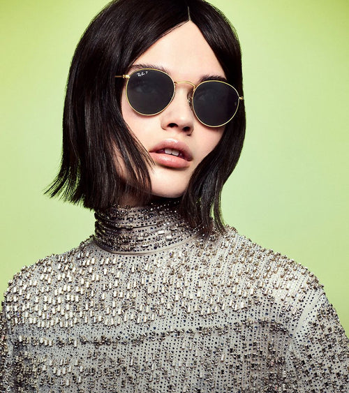 A young man with curly hair wears stylish sunglasses outdoors.
