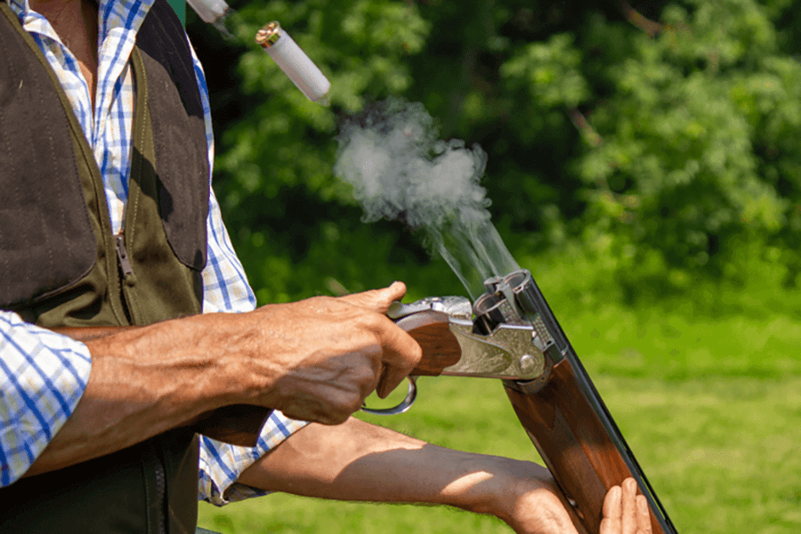 Person holding a shotgun with smoke coming from the barrel outdoors.