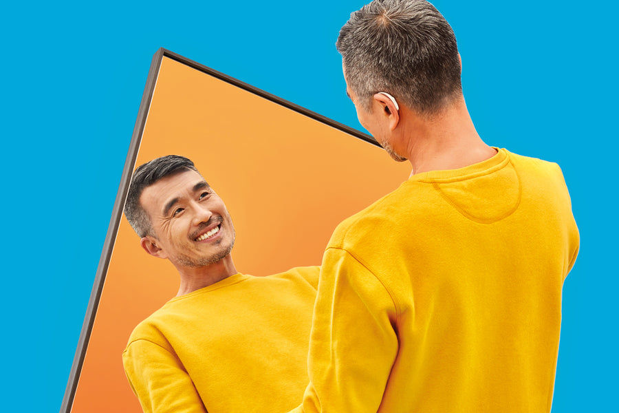 A woman in a black outfit poses by a mirror while a man stands behind.