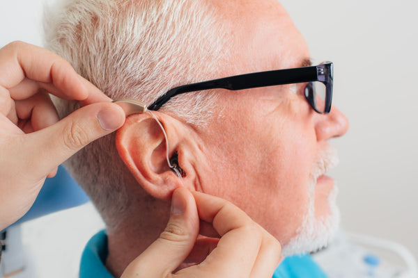 Person fitting a hearing aid into an elderly person's ear.