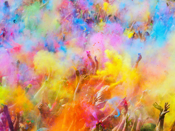 Crowd celebrating with vibrant colored powder clouds during a festive outdoor event.