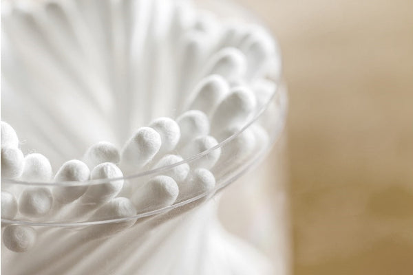 Close-up of white cotton swabs arranged in a clear glass container with a beige background.
