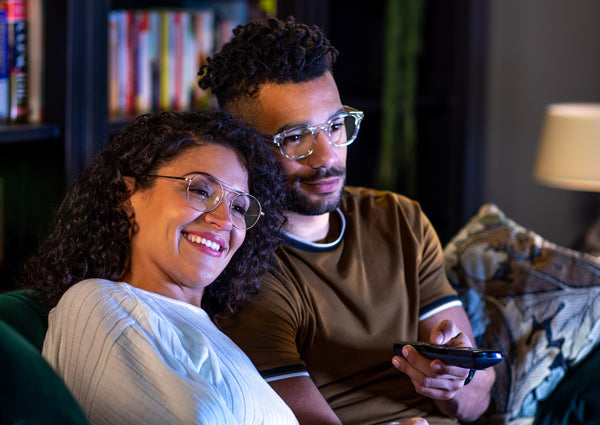 Couple sitting on a couch watching TV, with one person holding a remote control in a cozy living room setting.