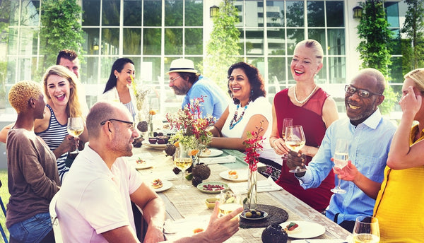 Group of diverse adults enjoying an outdoor meal together, smiling and toasting with wine glasses around a decorated table.