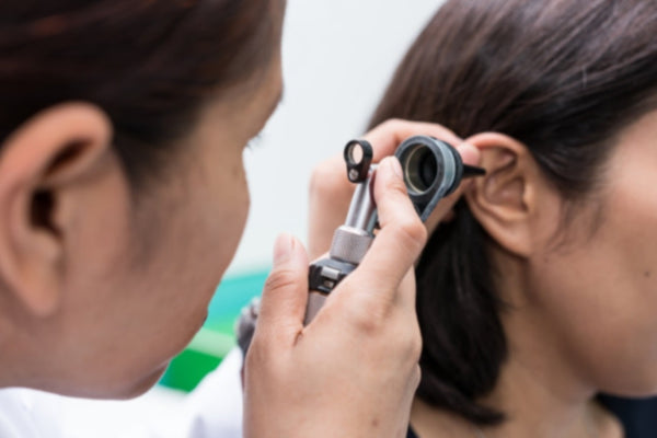 Healthcare professional examining a patient's ear using an otoscope during a medical check-up.