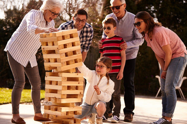 Family playing a giant outdoor Jenga game together on a sunny day with multiple generations enjoying the activity.
