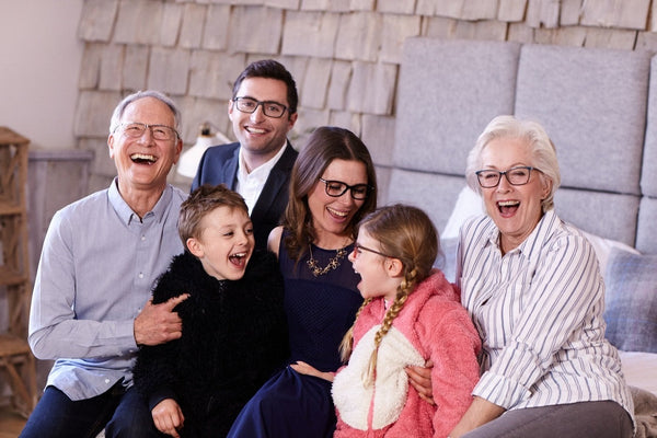 A multi-generation family sitting together on a bed, laughing and enjoying quality time in a cozy, warmly lit room.