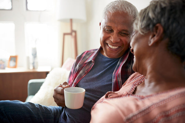 Two people sitting closely on a couch, sharing a warm moment with one holding a white coffee mug in a cozy living room.