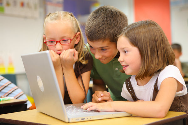 Three children gathered around a laptop in a classroom, engaged and focused on the screen.