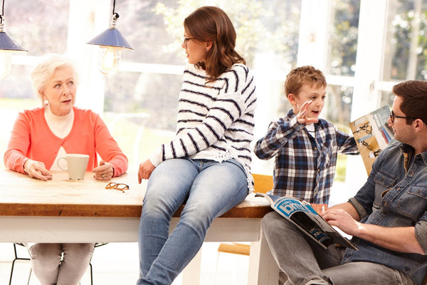 Family members engaging in conversation and reading magazines around a bright kitchen table with hanging lights.