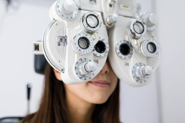Eye examination using a phoropter device to test vision and determine eyewear prescription in an optometry clinic.