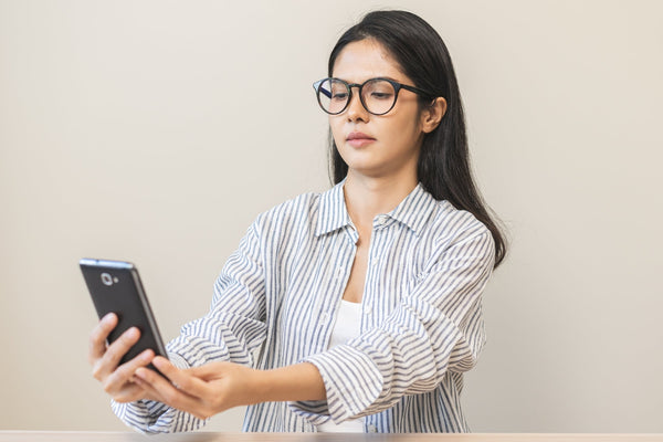 Person wearing glasses and striped shirt holding a smartphone with both hands against a plain background.