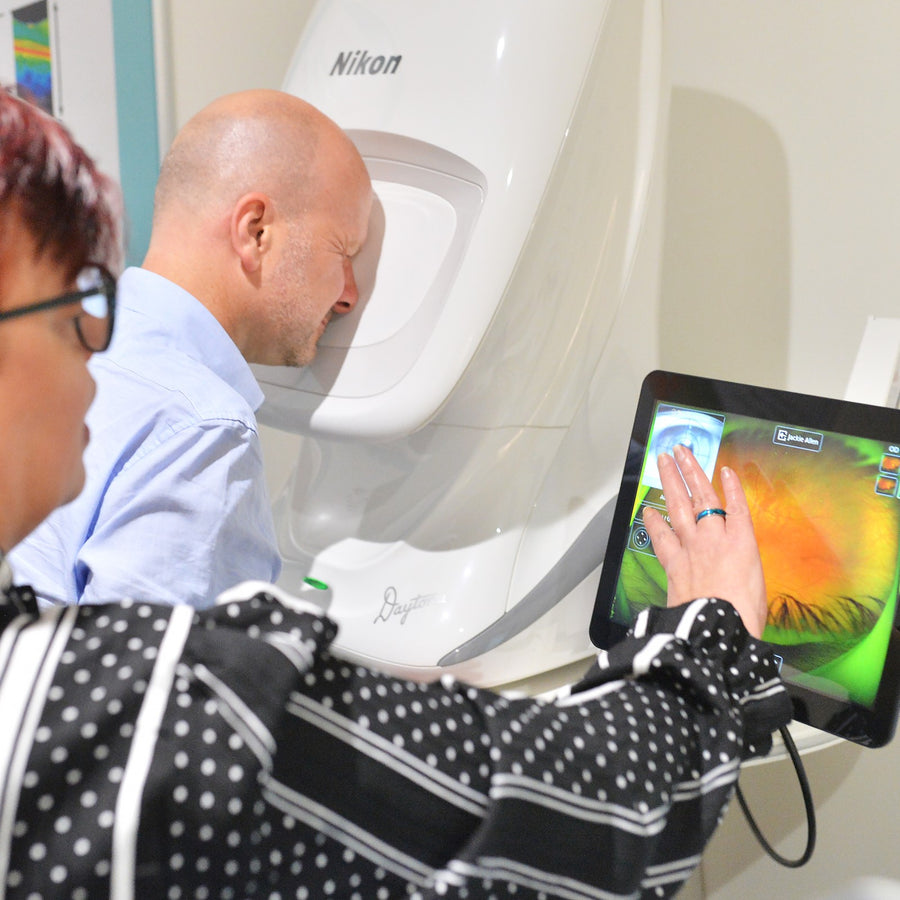 Person using the touch screen of the Optomap medical imaging device, with the device visible in the background.