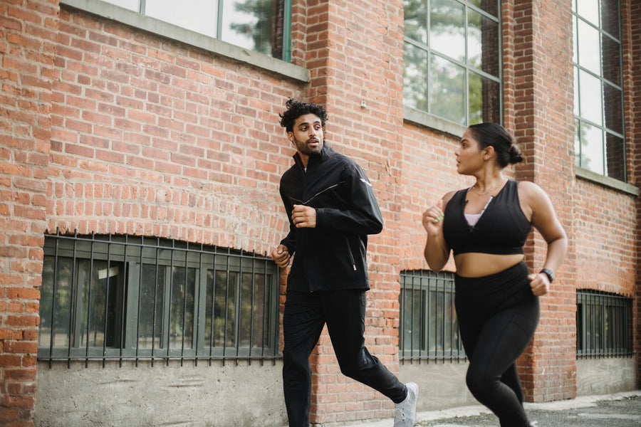 Two people running outdoors in front of a brick building