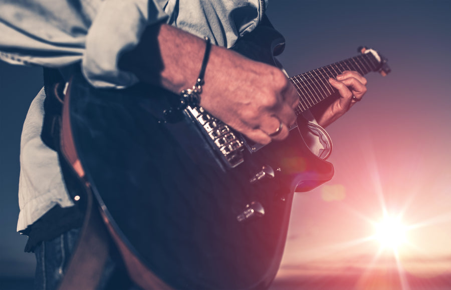 Person playing electric guitar outdoors during sunset with lens flare and soft lighting effects.