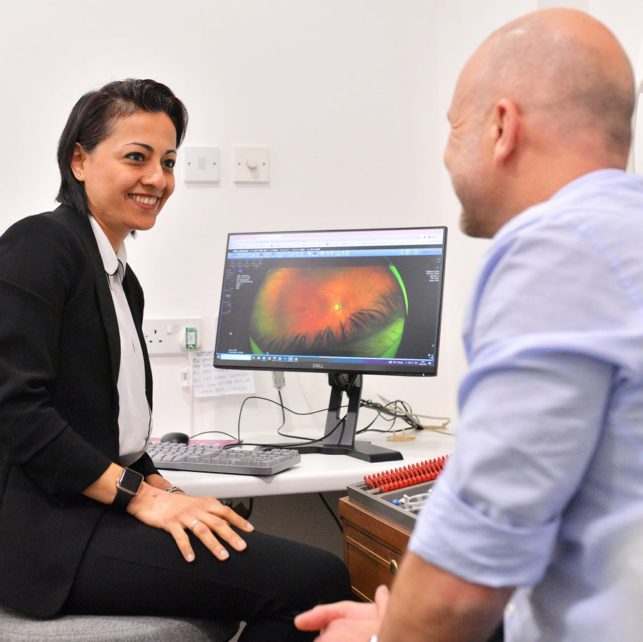 Person interacting with a computer screen displaying an eye scan in a clinical setting.