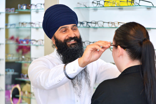 Man adjusting glasses for a woman in an eyewear store.
