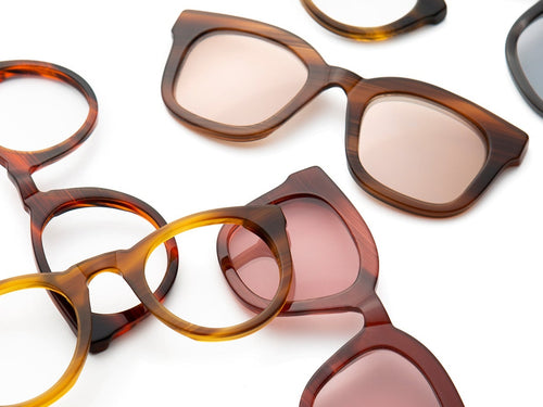 Assorted stylish eyeglass frames and sunglasses in various tortoiseshell and brown tones arranged on a white background.