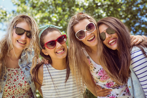Four women wearing sunglasses and smiling outdoors.