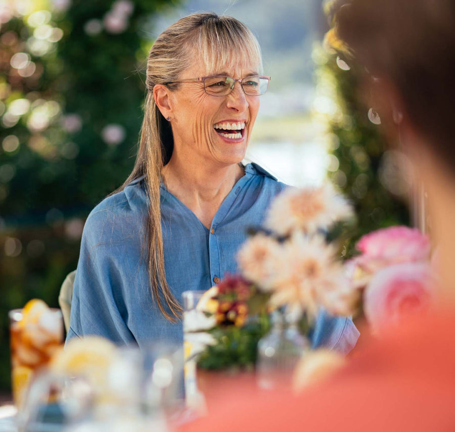 Woman laughing outdoors at a table.