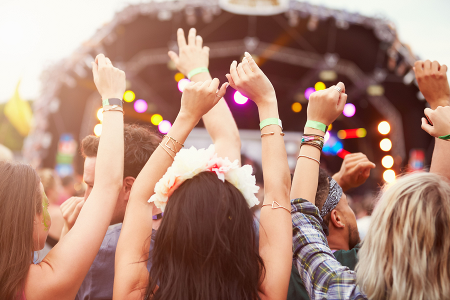 Crowd raising hands at a vibrant summer music festival with colorful stage lights and smoke effects.