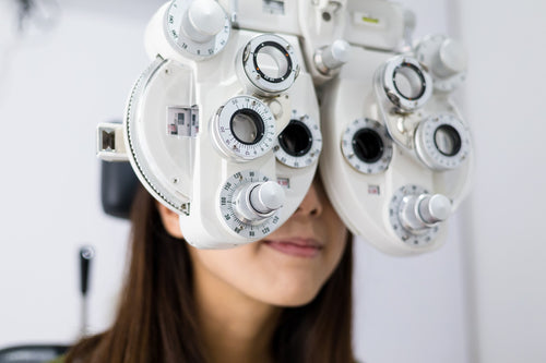 Eye examination using a phoropter device to test vision and determine eyewear prescription in an optometry clinic.