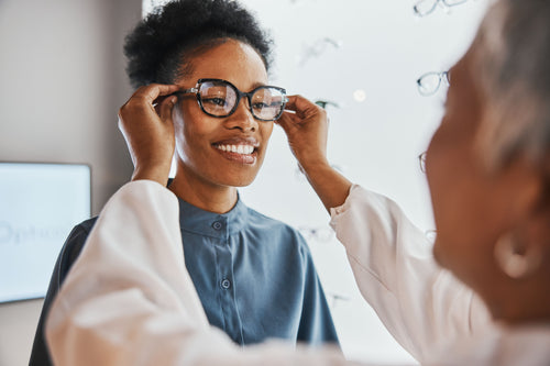 Customer trying on eyeglasses while an optician adjusts the frames at an optical store.