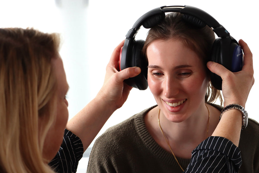A woman adjusting headphones on another woman’s head.